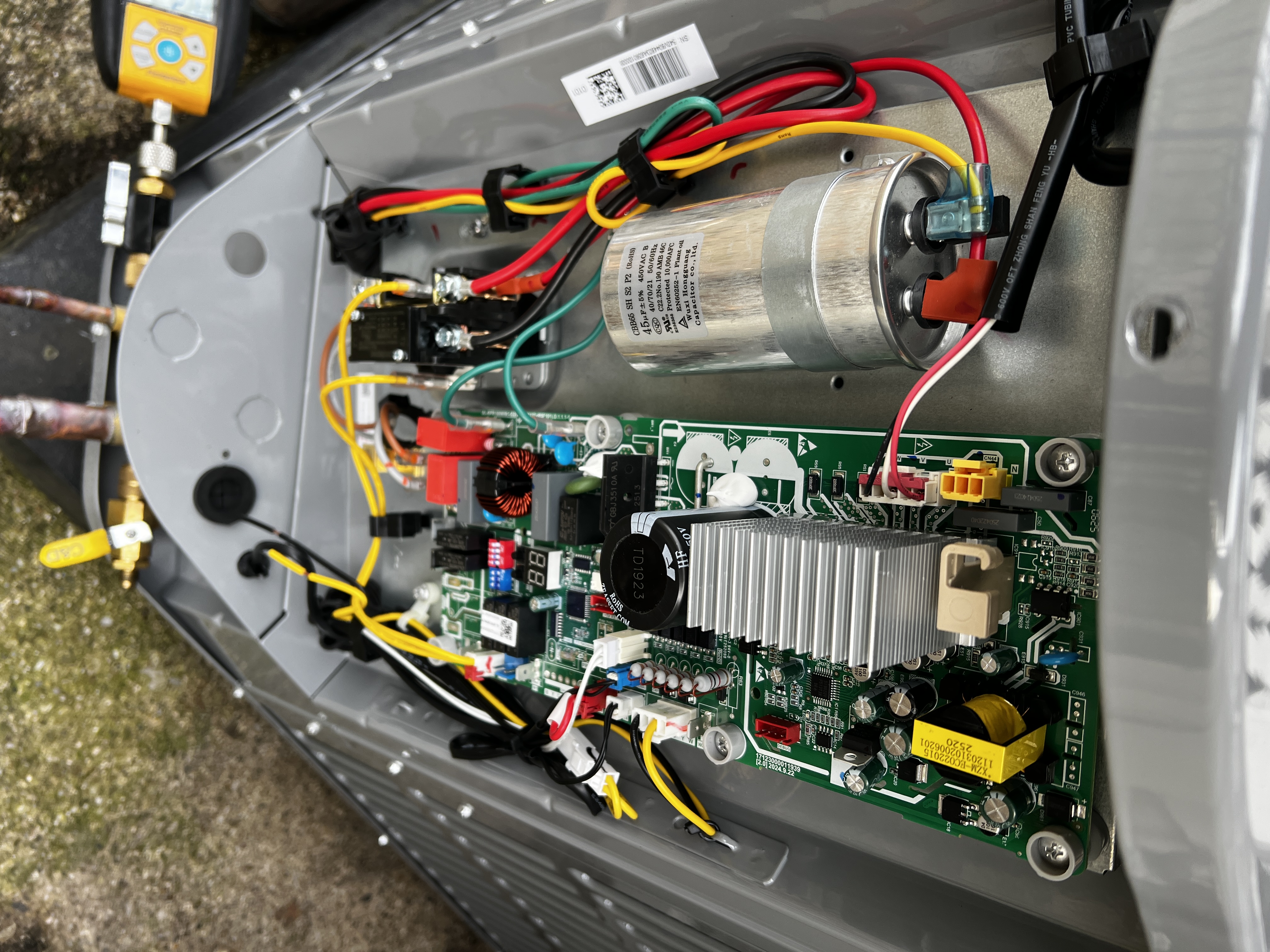 Close-up of an outdoor unit control board, capacitor, and electrical wiring with the service panel removed
