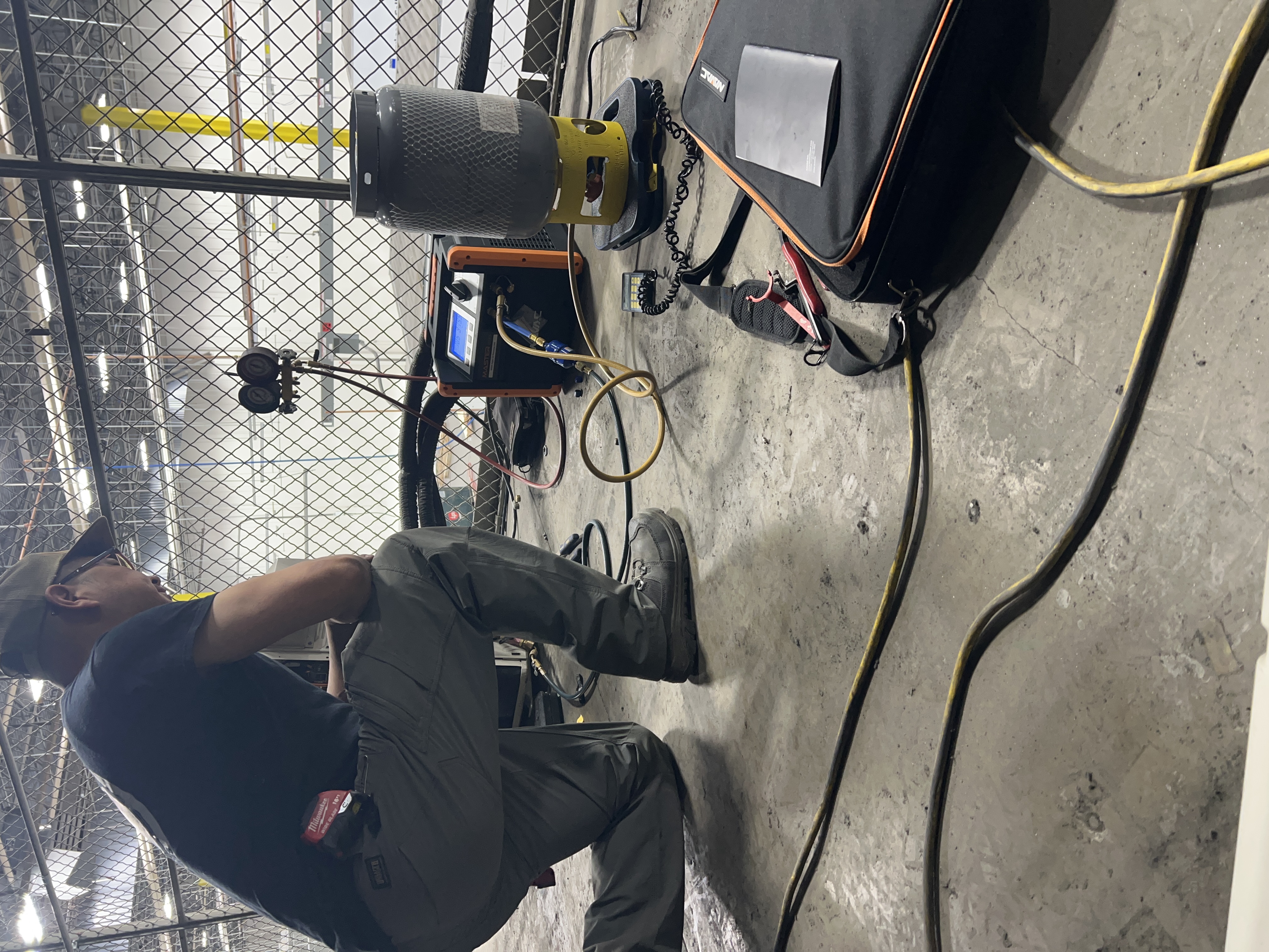 Technician working with refrigerant gauges, recovery equipment, and a cylinder